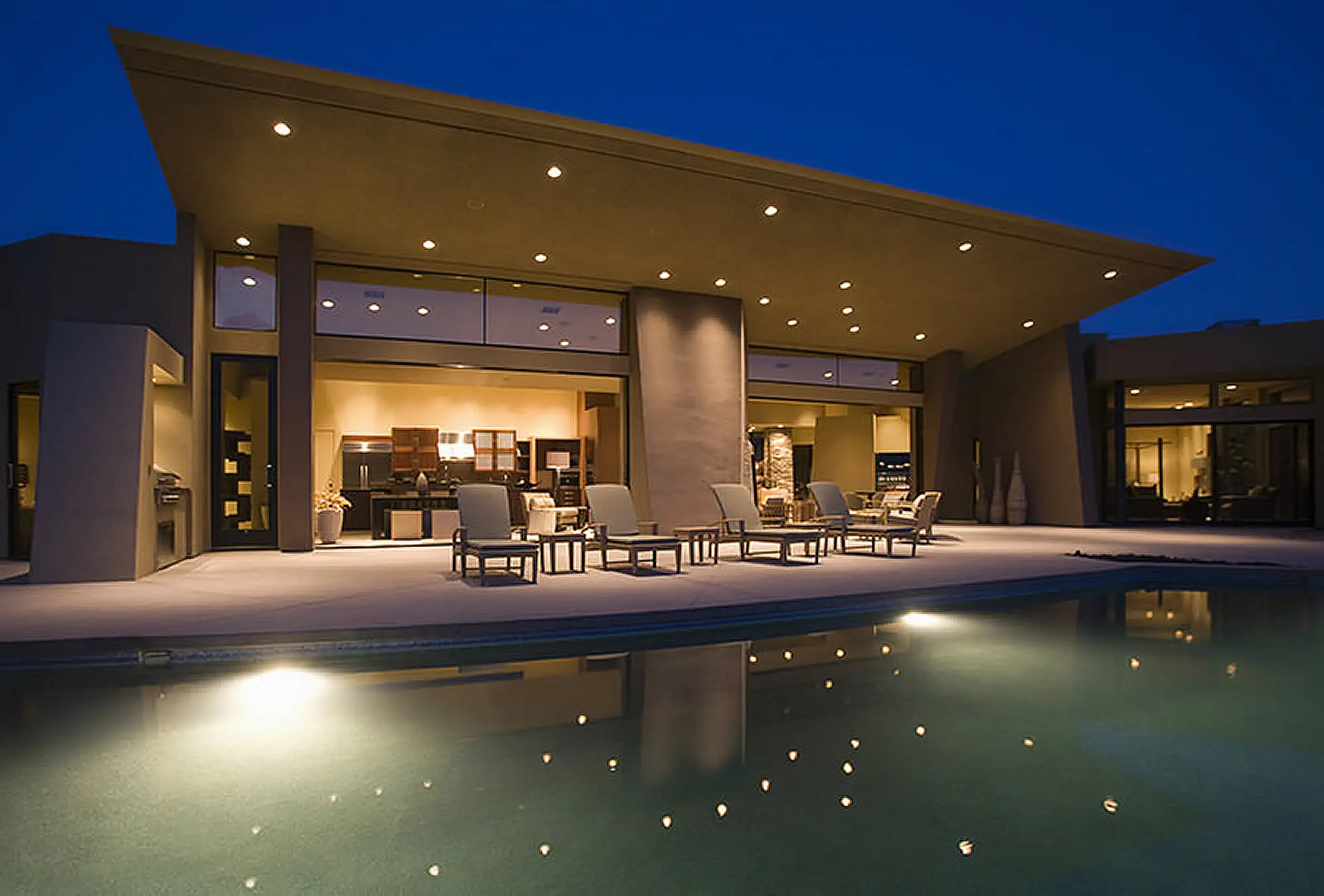 Modern desert home exterior with illuminated patio and pool at night